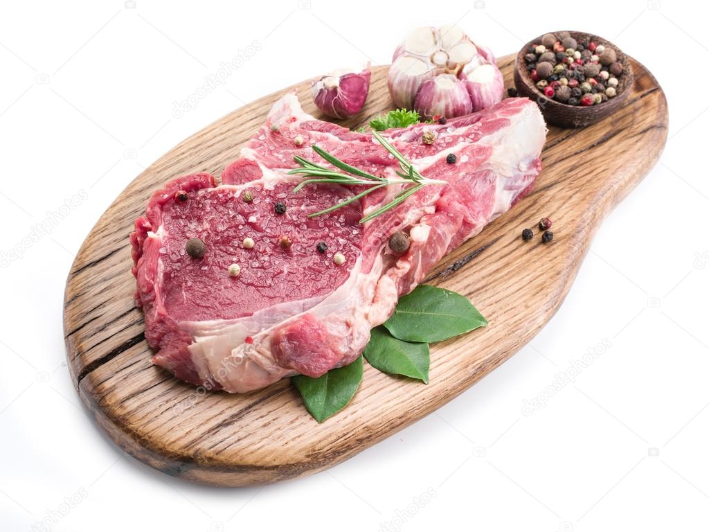 Beef steak with spices on the wooden cutting board.