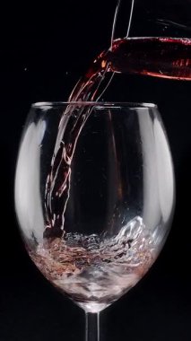 Kırmızı şarabın siyah arka plandaki berrak bir bardağa dökülüşünün yavaş çekimleri. Zarif sıvı hareket, zengin renk ve şarabın dokusunun makro detaylarla yakalanması..