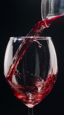Kırmızı şarabın siyah arka plandaki berrak bir bardağa dökülüşünün yavaş çekimleri. Zarif sıvı hareket, zengin renk ve şarabın dokusunun makro detaylarla yakalanması..