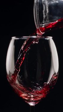 Kırmızı şarabın siyah arka plandaki berrak bir bardağa dökülüşünün yavaş çekimleri. Zarif sıvı hareket, zengin renk ve şarabın dokusunun makro detaylarla yakalanması..