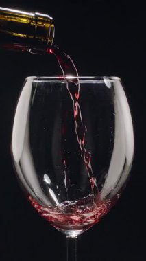 Kırmızı şarabın siyah arka plandaki berrak bir bardağa dökülüşünün yavaş çekimleri. Zarif sıvı hareket, zengin renk ve şarabın dokusunun makro detaylarla yakalanması..