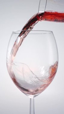 Pembe şarabın beyaz arka planda temiz bir bardağa dökülüşünün yavaş çekimleri. Lüks konsepti, şarap tatma, kutlama, güzel yemekler, restoran atmosferi ve alkol kültürü..