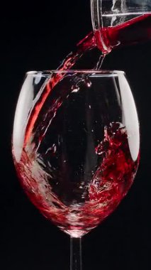 Kırmızı şarabın siyah arka plandaki berrak bir bardağa dökülüşünün yavaş çekimleri. Zarif sıvı hareket, zengin renk ve şarabın dokusunun makro detaylarla yakalanması..