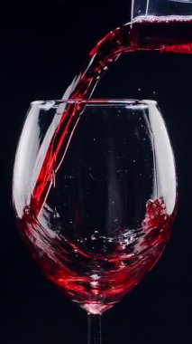 Kırmızı şarabın siyah arka plandaki berrak bir bardağa dökülüşünün yavaş çekimleri. Zarif sıvı hareket, zengin renk ve şarabın dokusunun makro detaylarla yakalanması..