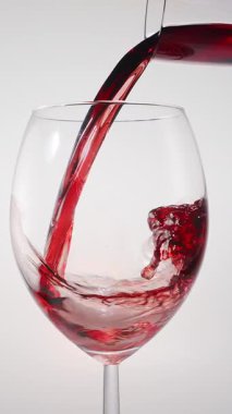 Kırmızı şarabın beyaz arka planda temiz bir bardağa dökülüşünün yavaş çekim görüntüsü. Zarif sıvı hareket, zengin renk ve şarabın dokusunun makro detaylarla yakalanması..