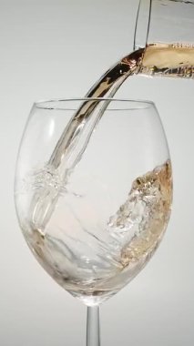 Beyaz arka planda beyaz bir bardağa dökülen beyaz şarabın yavaş çekimde yakın çekimi. Şarabın zarif sıvı hareketi makro ayrıntılarda yakalanır. Lüks konsepti, şarap tatma, kutlama, güzel yemekler, restoran atmosferi ve alkol kültürü..