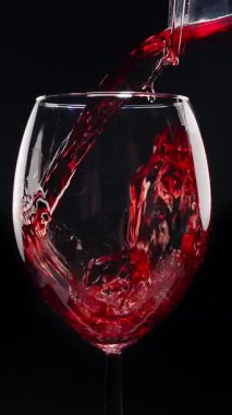 Kırmızı şarabın siyah arka plandaki berrak bir bardağa dökülüşünün yavaş çekimleri. Zarif sıvı hareket, zengin renk ve şarabın dokusunun makro detaylarla yakalanması..