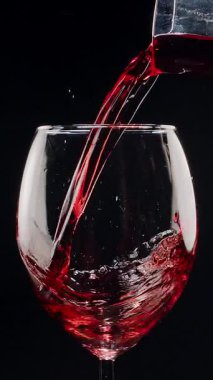 Kırmızı şarabın siyah arka plandaki berrak bir bardağa dökülüşünün yavaş çekimleri. Zarif sıvı hareket, zengin renk ve şarabın dokusunun makro detaylarla yakalanması..