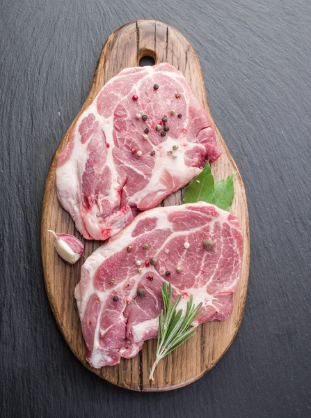 Bife de porco cru com especiarias na placa de corte preta . — Fotografia de Stock