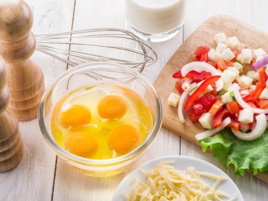 Omlet malzemeler: yumurta, taze kesilmiş sebzeler, süt ve peynir üzerinde ahşap masa.