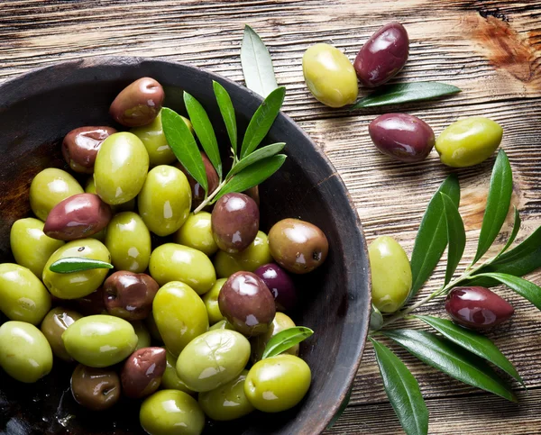 Tigela de madeira cheia de azeitonas e ramos de oliveira além dele . — Fotografia de Stock