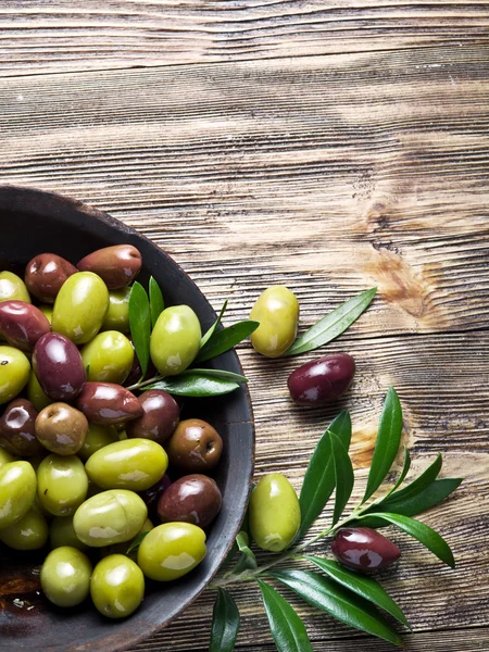 Houten kom vol van olijven en olijfolie twijgen naast het. — Stockfoto