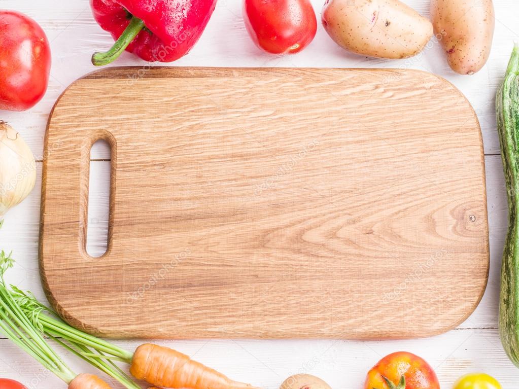 Wooden empty chopping board and vegetables near it.
