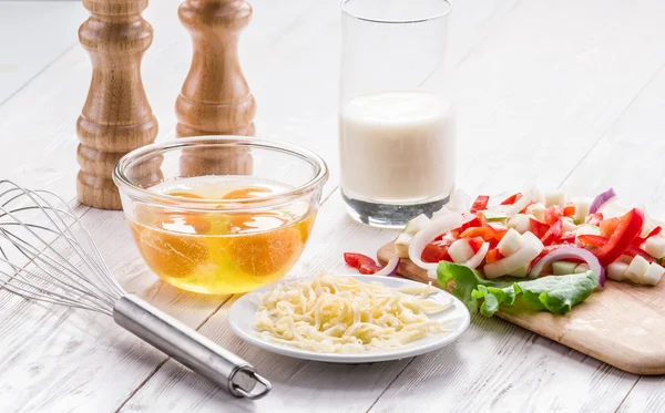 Omelette ingredients: eggs, fresh cut vegetables, milk and cheese on the wooden table.