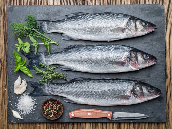 Peixe-marinho sobre uma placa de grafite com especiarias e ervas . — Fotografia de Stock