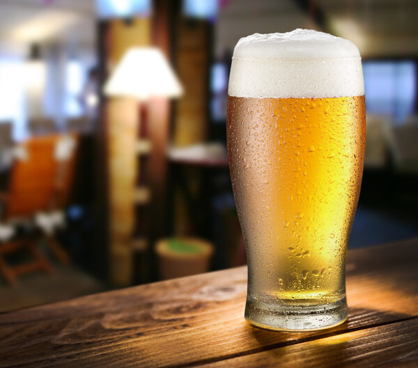 Glass of light beer on the glass bar counter.