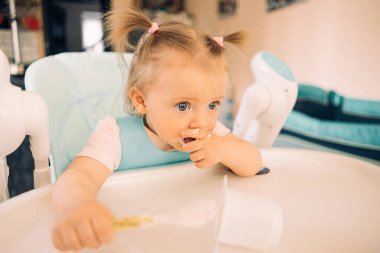 Mutfakta, masada, çocuk sandalyesinde yoğurt yiyen bir kız çocuğu.