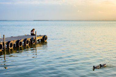 İskelede, kadın sırtüstü oturuyor.