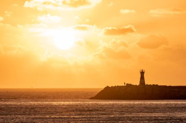 Portekiz 'de gün batımında bulutlu bir günde arka planda kule ve taşlarla Atlantik kıyısı