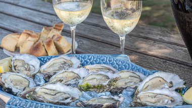 Seramik tabakta hazır taze istiridye ve şarap bardakları açık hava restoranında koyu ahşap arka planda şampanya.