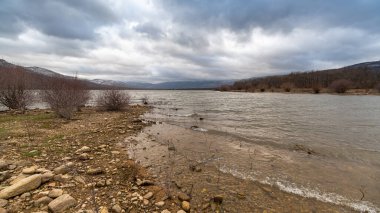 Madrid, İspanya 'da bulutlu gökyüzü ve Sierra dağlarıyla Lozoya del Valle rezervuarı