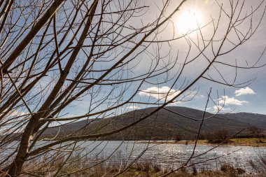 Güneşli bir günde, gün batımında bir göldeki dağların manzarası... Hasır çalıların siluetiyle...