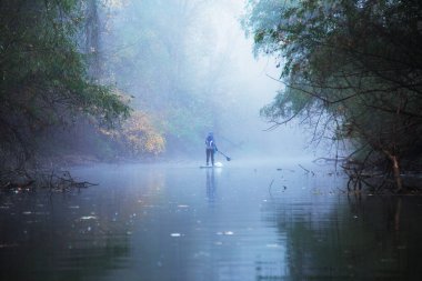 Sis dolu ağaçların altında, nehir kıyısındaki yemek masasında yüzen kürekçi, tanınmayan bir kadın.