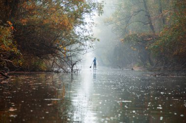 Sis dolu ağaçların altında, nehir kıyısındaki yemek masasında yüzen kürekçi, tanınmayan bir kadın.
