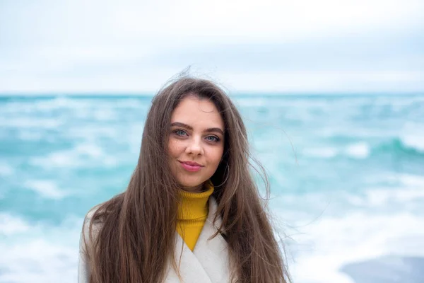 年轻的高加索黑发女子 蓝眼睛 望着冬季多风的海滩 背景是碧绿的海浪 — 图库照片