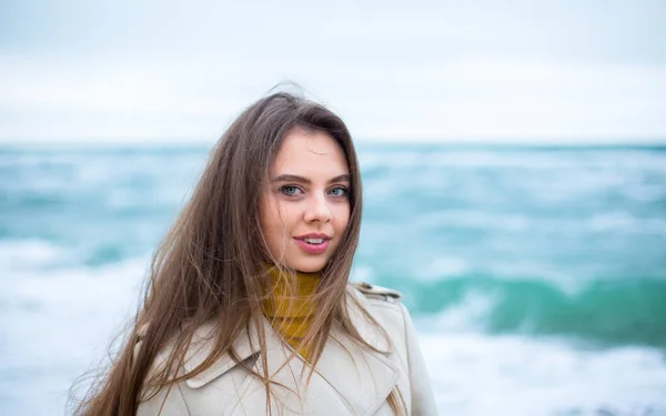 年轻的高加索黑发女性 蓝眼睛 在冬季的风沙海滩上 背景是碧绿的海浪 — 图库照片