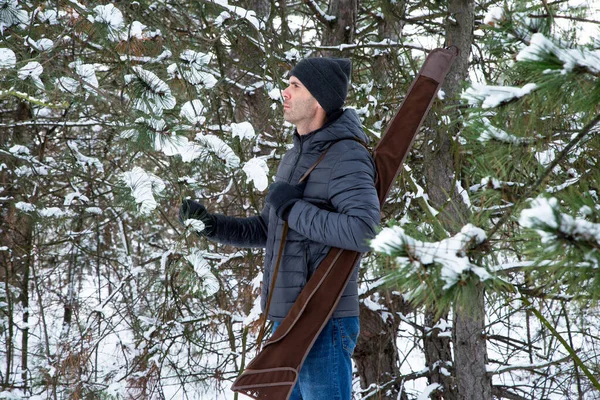 冬の森の肩に散弾銃を持ったダウンジャケットとジーンズの白人男性 — ストック写真