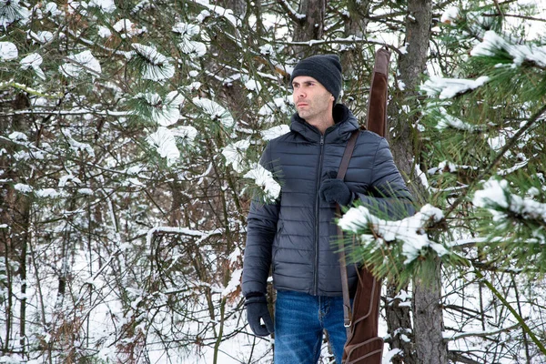 冬の森の肩に散弾銃を持ったダウンジャケットとジーンズの男 — ストック写真