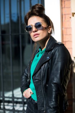 Siyah deri ceketli, şortlu ve şık güneş gözlüklü kadın kapalı dükkanın yanındaki merdivenlerde kalıyor.