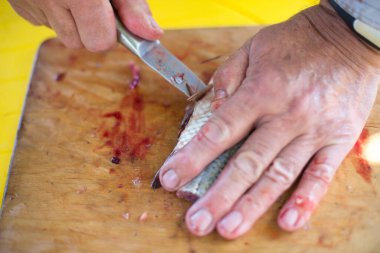 Adamın elleri teraziyi temizliyor ve bıçakla taze bir balığı kesiyor.