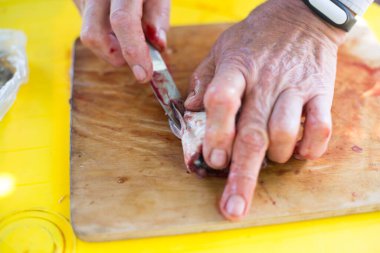 Adamın elleri teraziyi temizliyor ve bıçakla taze bir balığı kesiyor.