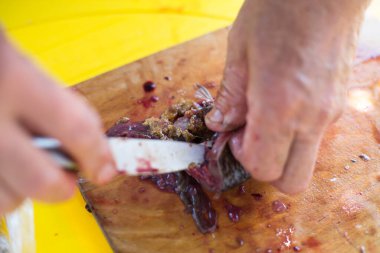 Adamın elleri teraziyi temizliyor ve bıçakla taze bir balığı kesiyor.