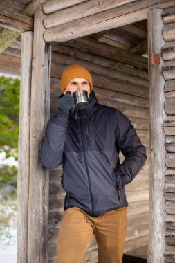 Ahşap bir orman kulübesinde beyaz erkek yürüyüşçü sıcak bir çay içiyor.