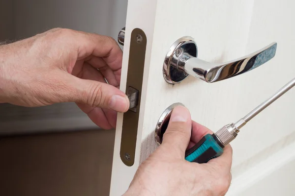 Worker installing or repairing new lock and door knob with screwdriver. Locksmith repair or install the door lock in house.