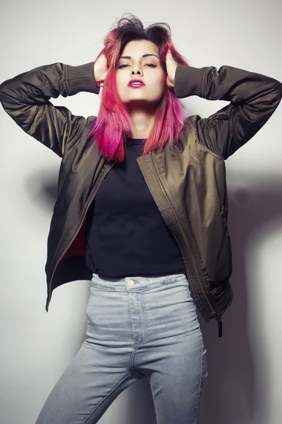 Mladá žena v bundě a modré džíny s růžovými vlasy studio shot — Stock fotografie