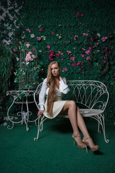 Mode und schöne junge Frau in einer grünen Wand aus Blumen und Blättern — Stockfoto