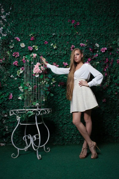 Mode und schöne junge Frau in einer grünen Wand aus Blumen und Blättern — Stockfoto