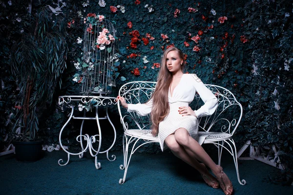 Moda y hermosa mujer joven en una pared verde de flores y hojas — Foto de Stock