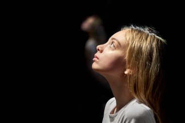 Genç bir kızın portresi. Siyah bir arka planda uzaktan bir yansımayla yukarı bakıyor.