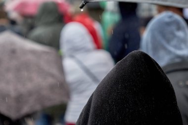 Kalabalıkta kapüşonlu bir adam sağanak yağmurda yürür.