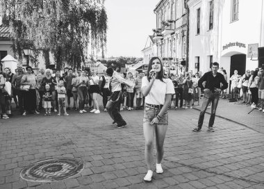 4 Ağustos 2018, Minsk Belarus. Mikrofonlu güzel bir kız şehrin caddesinde şarkı söylüyor. Siyah-beyaz görüntü.