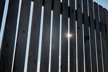 Güneşli bir yaz gününde ahşap bir çite yakın çekim. Güneş çitin içinden parlıyor