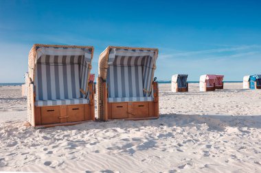 Sıcak yaz güneşinde kumsalda beyaz kumda duran çizgili hasır plaj sandalyeleri. Seyahat ve yaz tatili konsepti.