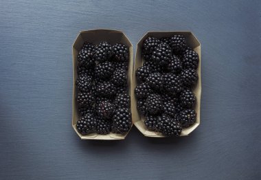 Gri arka planda taze toplanmış böğürtlenli iki karton kutunun üst görüntüsü. Taze meyve konseptinde vitaminler.