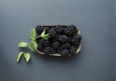 Kutunun üstünde taze böğürtlenler ve birkaç yapraklı yeşil dal var. Taze meyve konseptinde vitaminler.