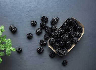 Üzerinde böğürtlen ve gri desenli masanın üzerinde duran diğer parçalarla kutunun üst görüntüsü. Taze meyve konseptinde vitaminler.